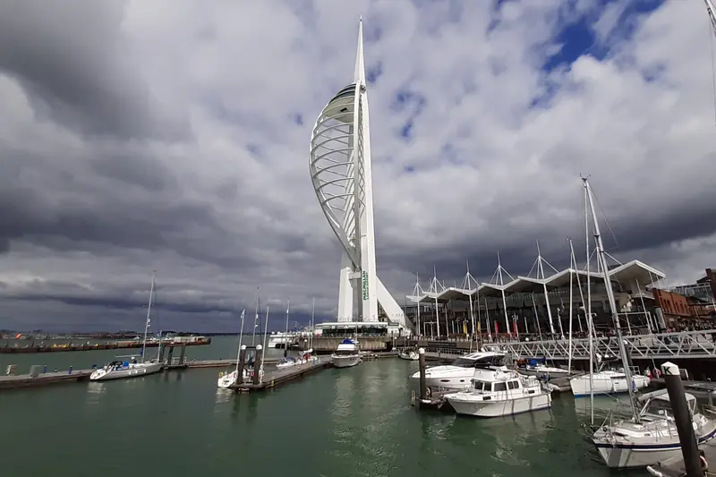The white sail-shaped Spinnaker Tower standing over pontoons of moored yachts and motor cruisers in Portsmouth Harbour beneath heavy grey cloud